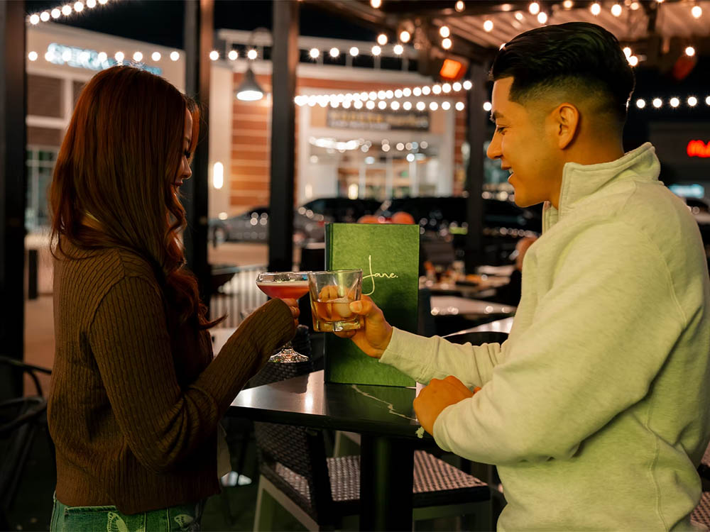 Couple toasting with cocktails from a personal liquor locker on the Jane Southlake patio at night