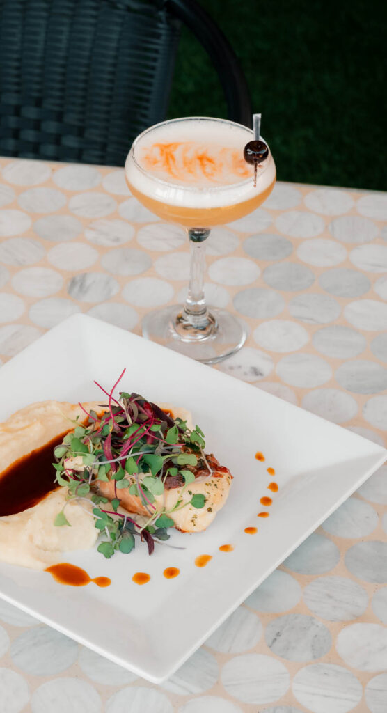 Plated entree with microgreens and a signature cocktail on the Jane Southlake patio