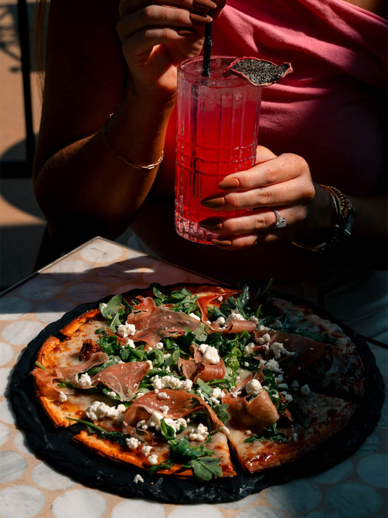 Prosciutto and goat cheese flatbread with arugula alongside a signature red cocktail at Jane Southlake